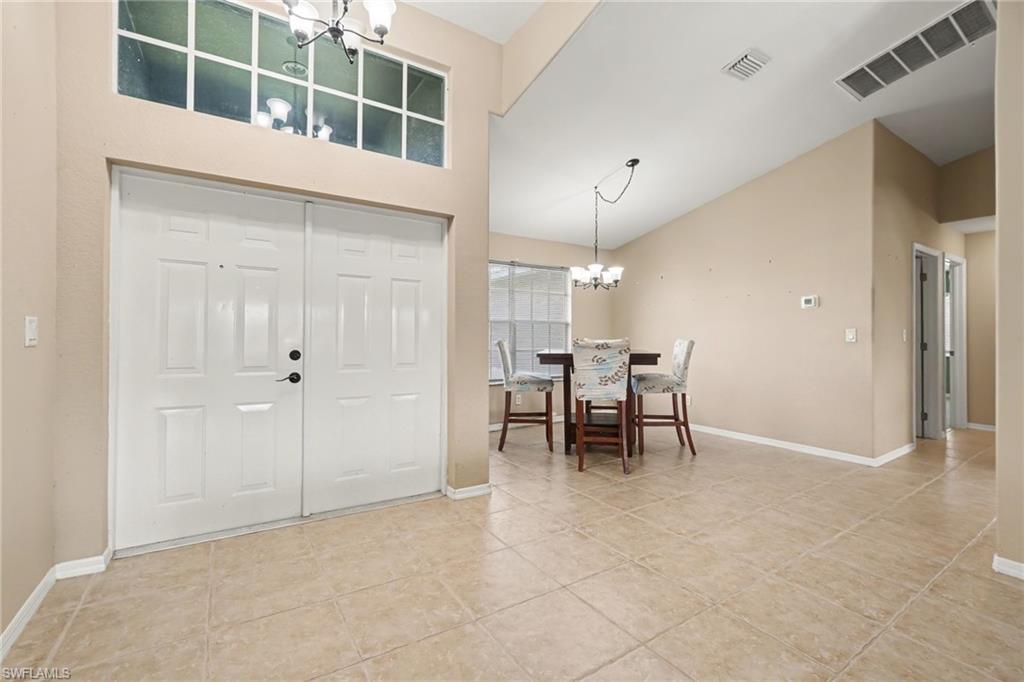 Double entry doors with transom window, tile flooring, vaulted ceilings, and a chandelier in the dining area