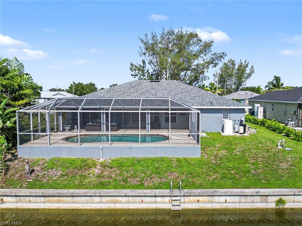 Rear exterior featuring a screened pool enclosure with an integrated swimming pool, seawall, and a shingled roof