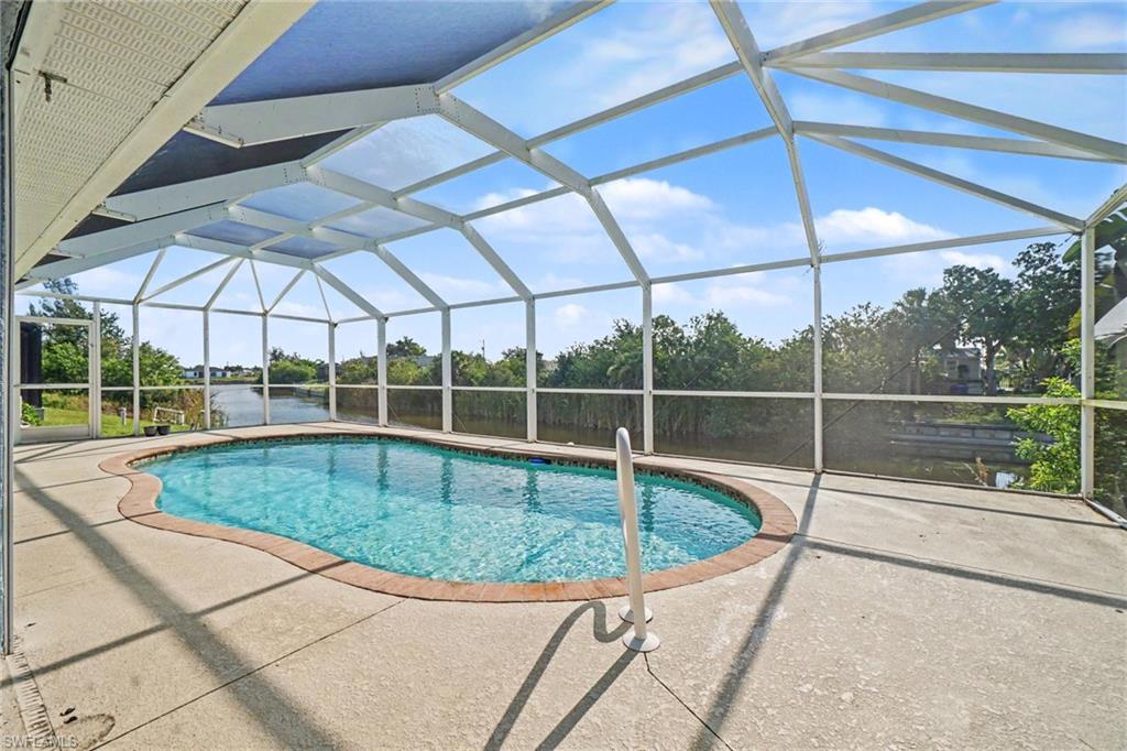 Screened pool area featuring a freeform swimming pool, concrete decking, and brick coping