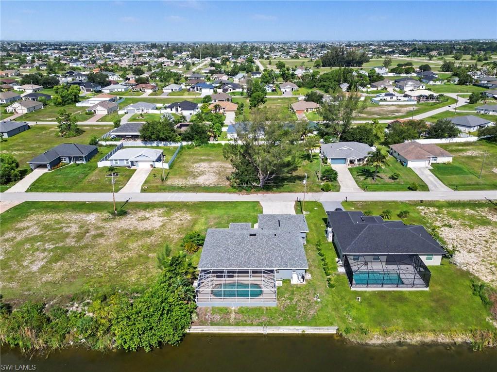 Waterfront property featuring a screened-in swimming pool, a spacious lawn, and mature landscaping