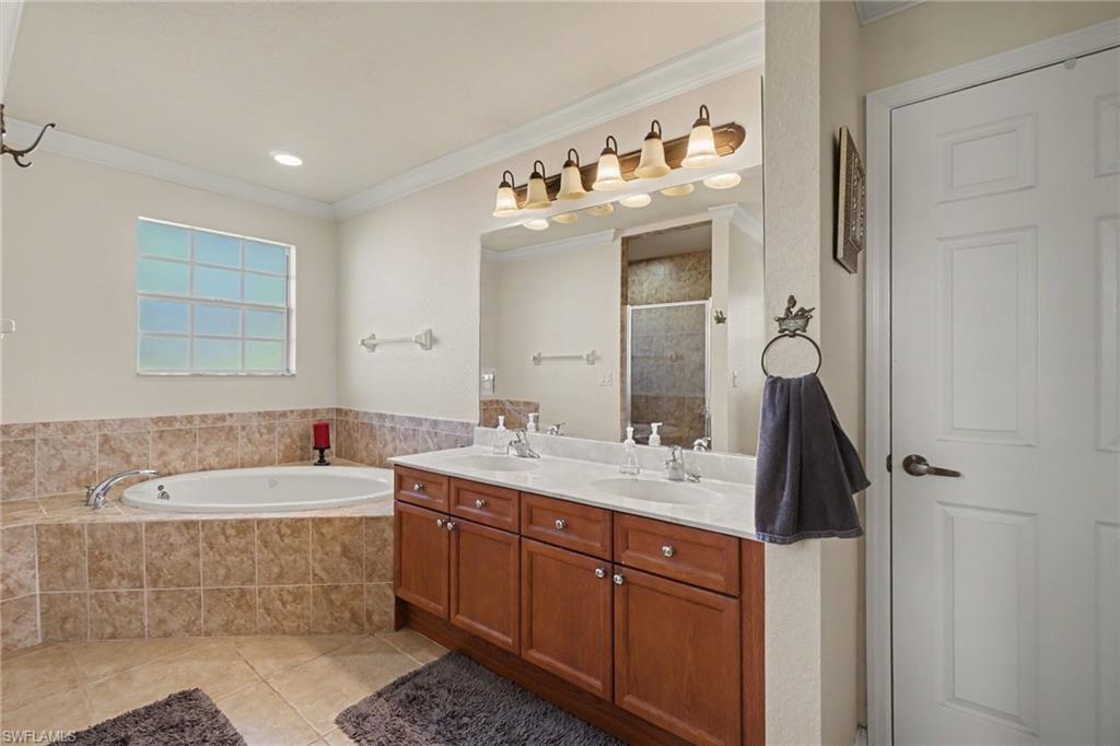 Bathroom featuring a large corner soaking tub with tiled surround, a double vanity with wood-finish cabinetry, a single window, and tiled flooring