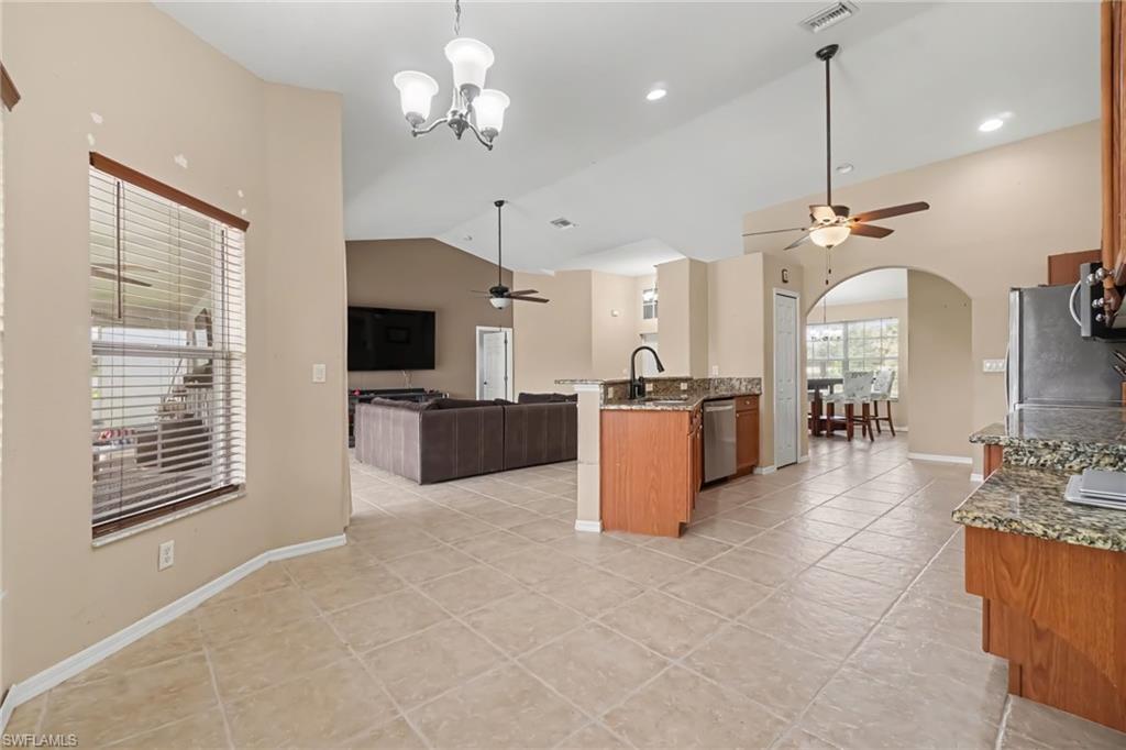 Spacious kitchen and living area featuring tile flooring, vaulted ceilings, a kitchen island with sink, granite countertops, and wood cabinetry
