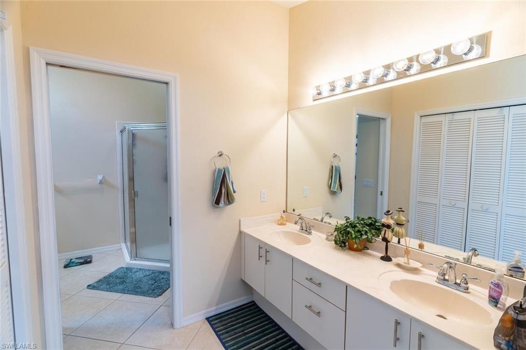 Full bath featuring double vanity, light tile patterned flooring, and a shower stall