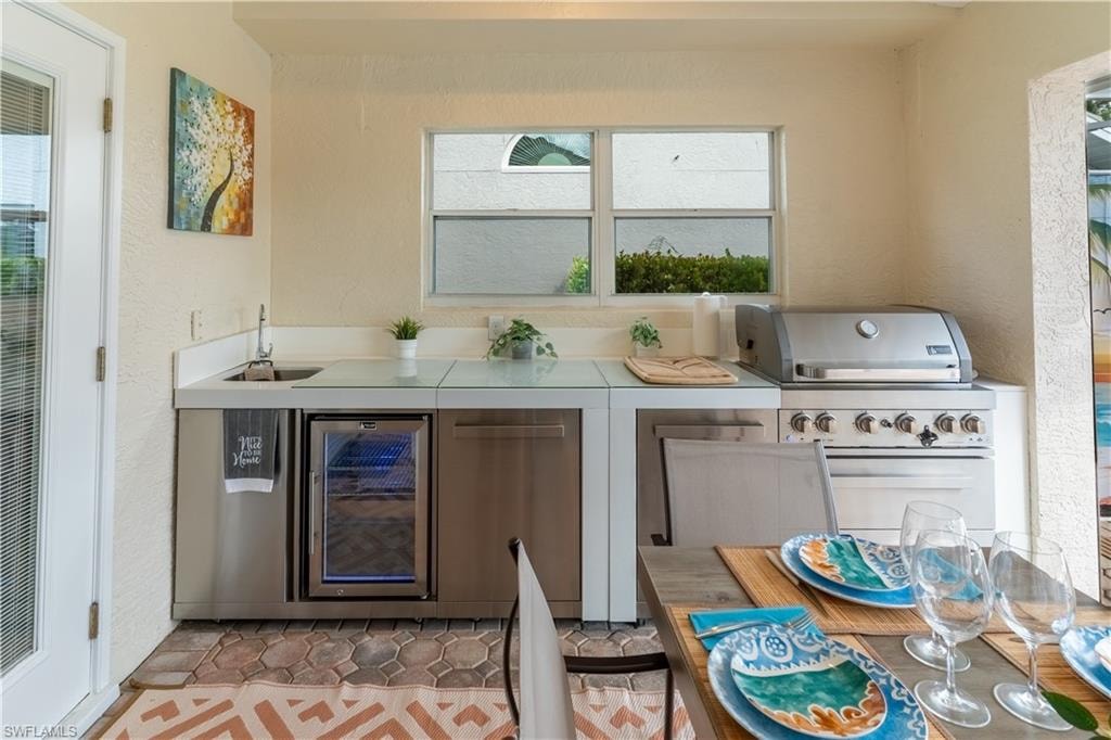 Bar area featuring a textured wall, light countertops, wine cooler, healthy amount of natural light, and light tile patterned floors
