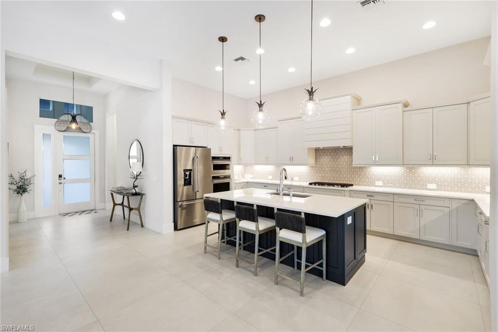Modern kitchen featuring light-toned cabinetry, stainless steel appliances, and a large central island with seating