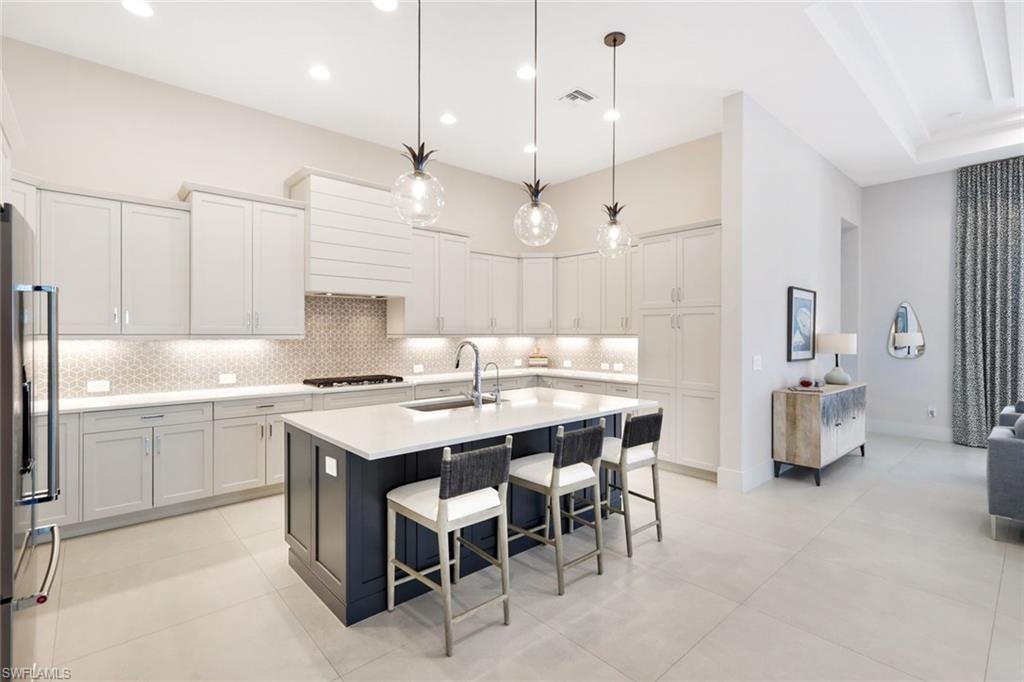 Modern kitchen featuring light cabinetry, a dark-toned island with seating, pendant lighting, and a geometric tile backsplash