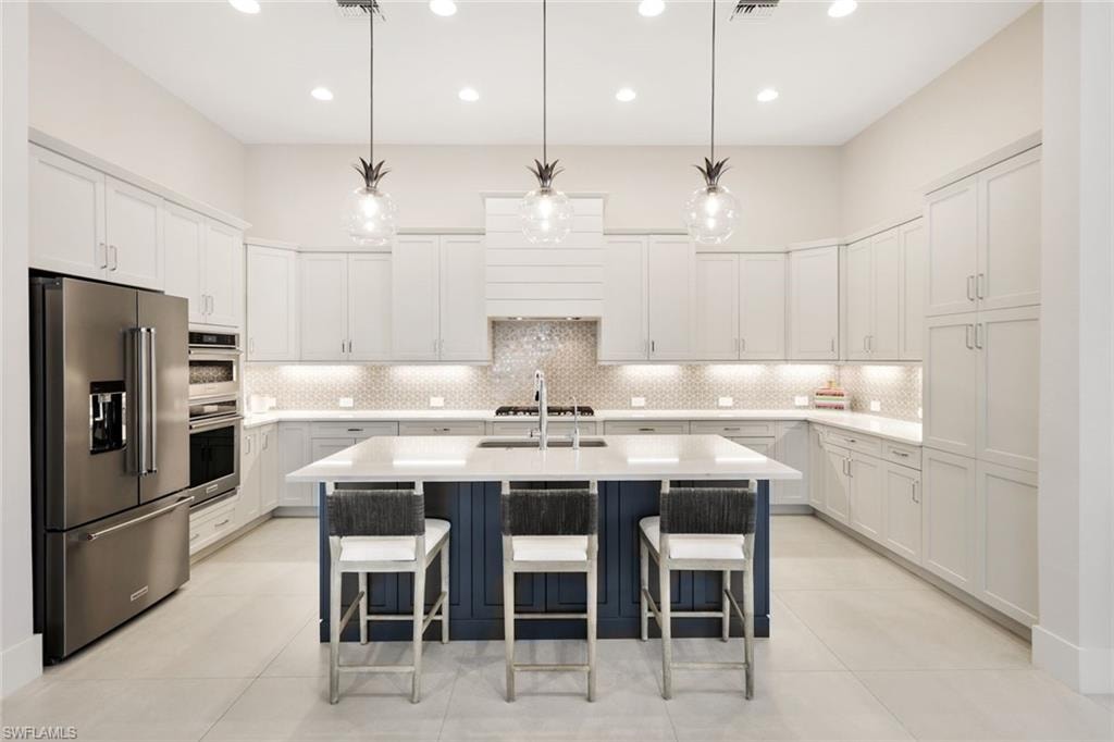 Modern kitchen featuring a large central island with a contrasting blue base, light countertops, and three pendant light fixtures