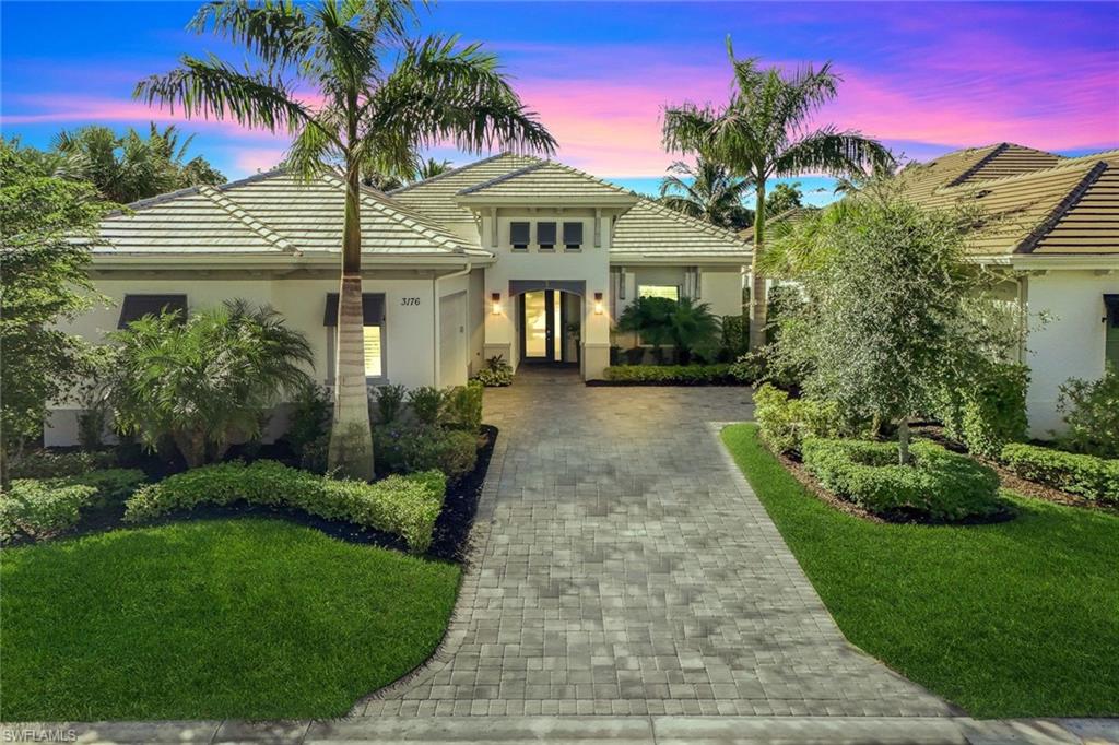 Contemporary architectural style featuring a tile roof, paver driveway, lush landscaping, exterior wall lighting, and an inviting entryway