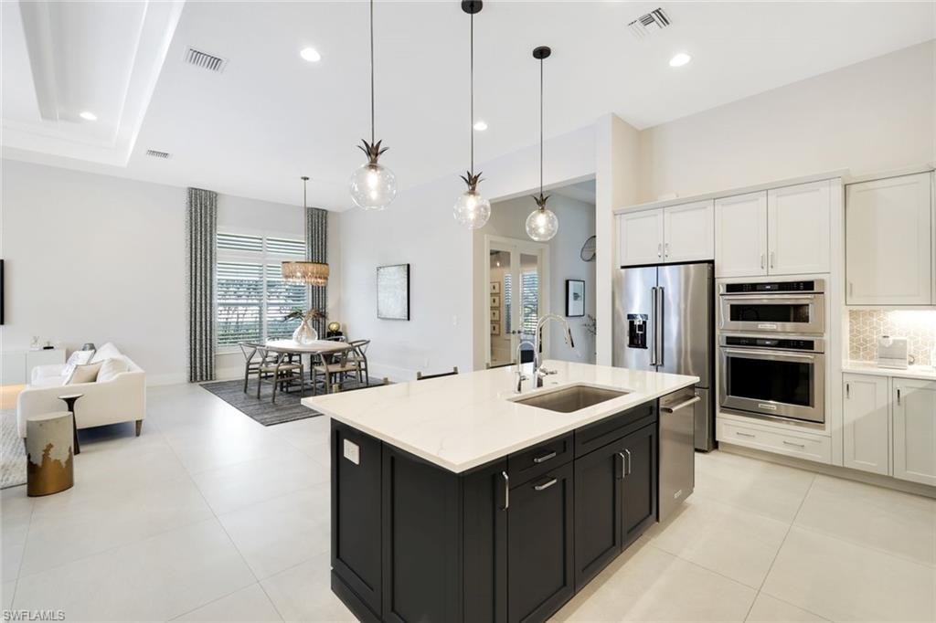 Gourmet kitchen featuring a large island with sink, stainless steel appliances, white cabinetry, and light-toned tile flooring