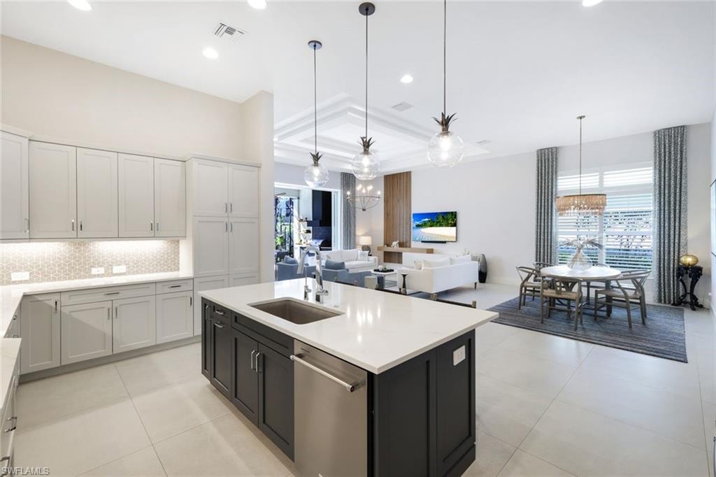 Open-concept living area featuring a kitchen island with sink and stainless steel dishwasher, light-toned cabinetry, high ceilings, and recessed lighting