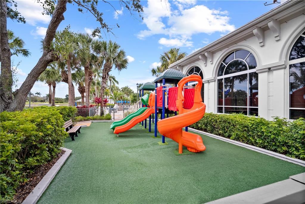 Recreational playground area featuring colorful play equipment, artificial turf surfacing, and lush perimeter landscaping