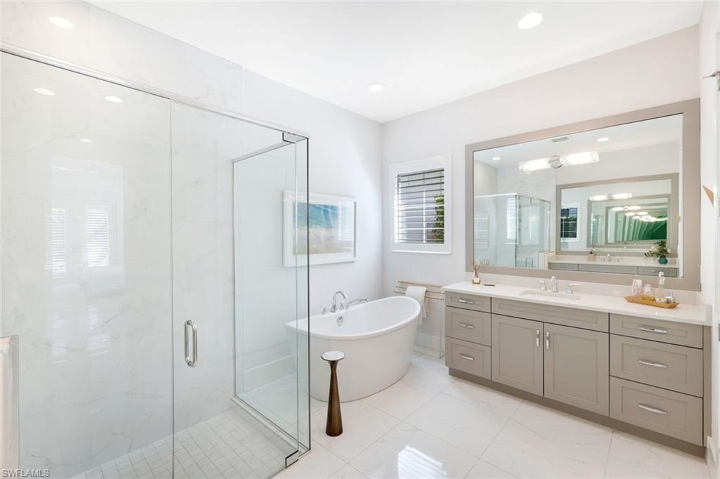 Spacious bathroom featuring a frameless glass shower enclosure, a freestanding soaking tub, an extended vanity with dual sinks, a large framed mirror, and recessed lighting