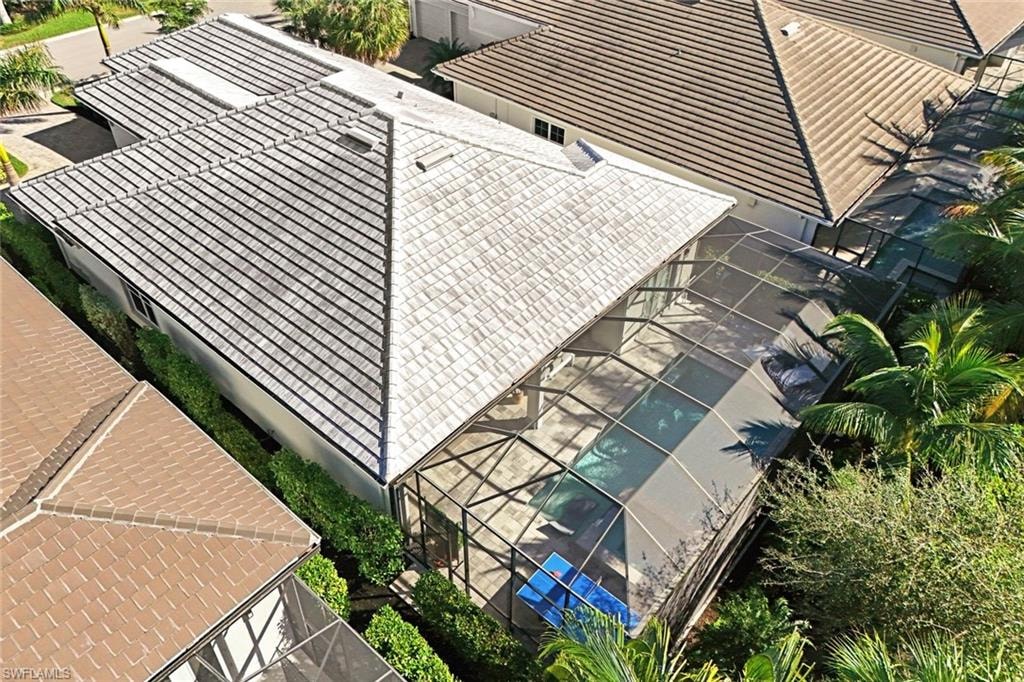 Residential property featuring a screened pool enclosure, tile roofing, and established landscaping