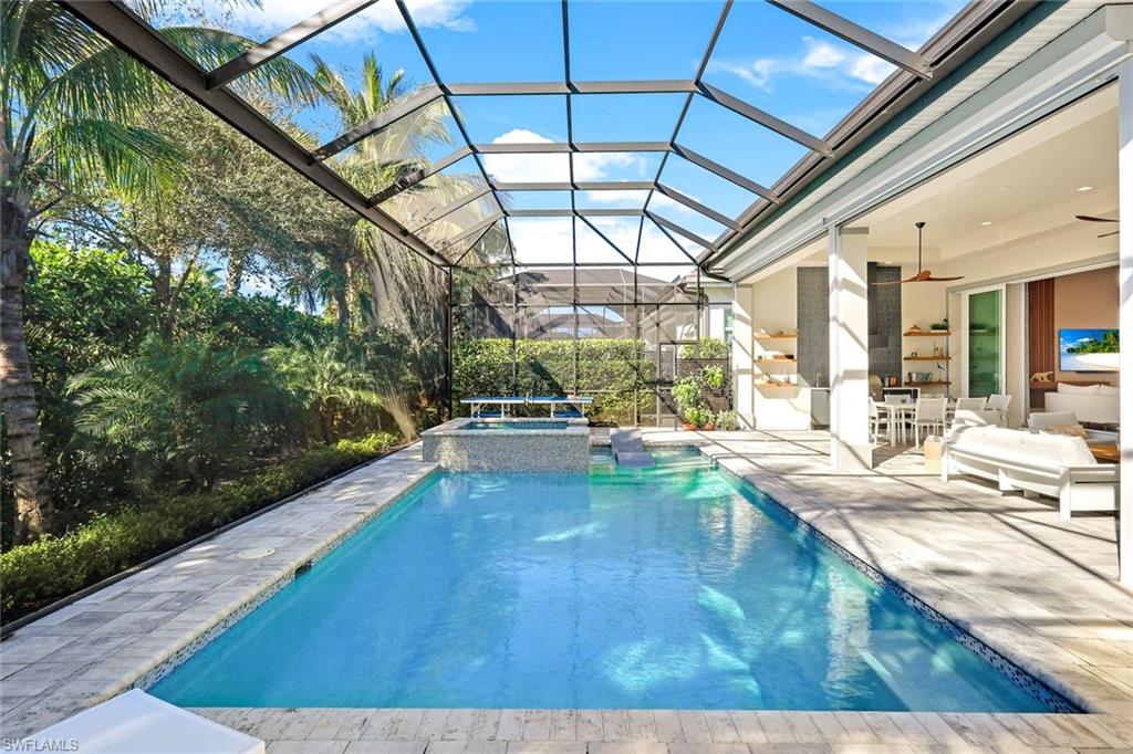Screened-in outdoor living space featuring a rectangular swimming pool with integrated spa, paver decking, and tropical landscaping