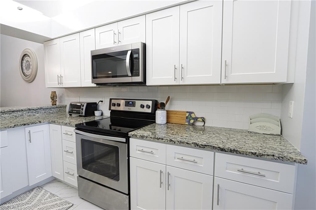 Kitchen with backsplash, light stone countertops, stainless steel appliances, and white cabinets