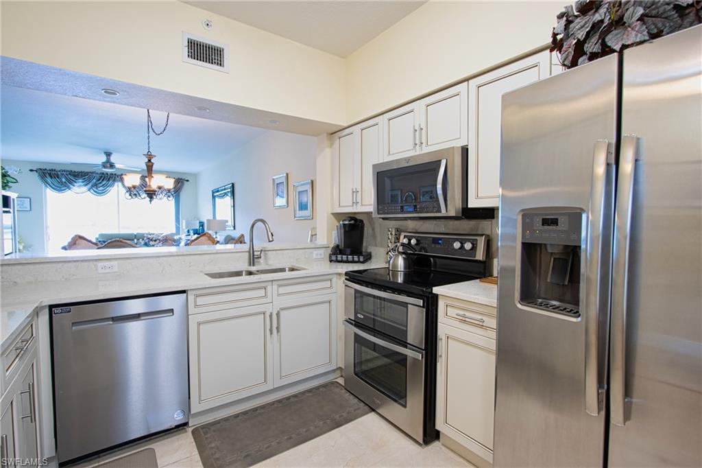 Kitchen featuring white cabinetry, light stone countertops, stainless steel appliances, sink, and light tile floors
