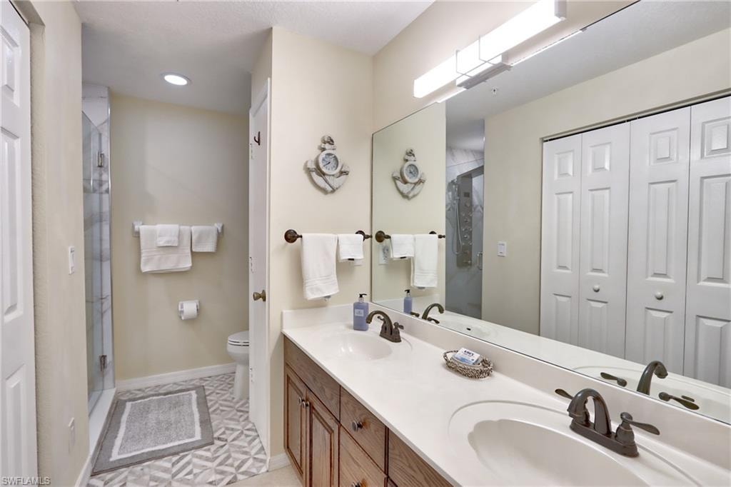 Bathroom featuring dual sinks, tile flooring, vanity with extensive cabinet space, a shower with door, and toilet