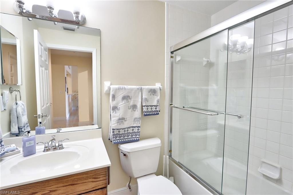 Full bathroom with enclosed tub / shower combo, vanity, and toilet