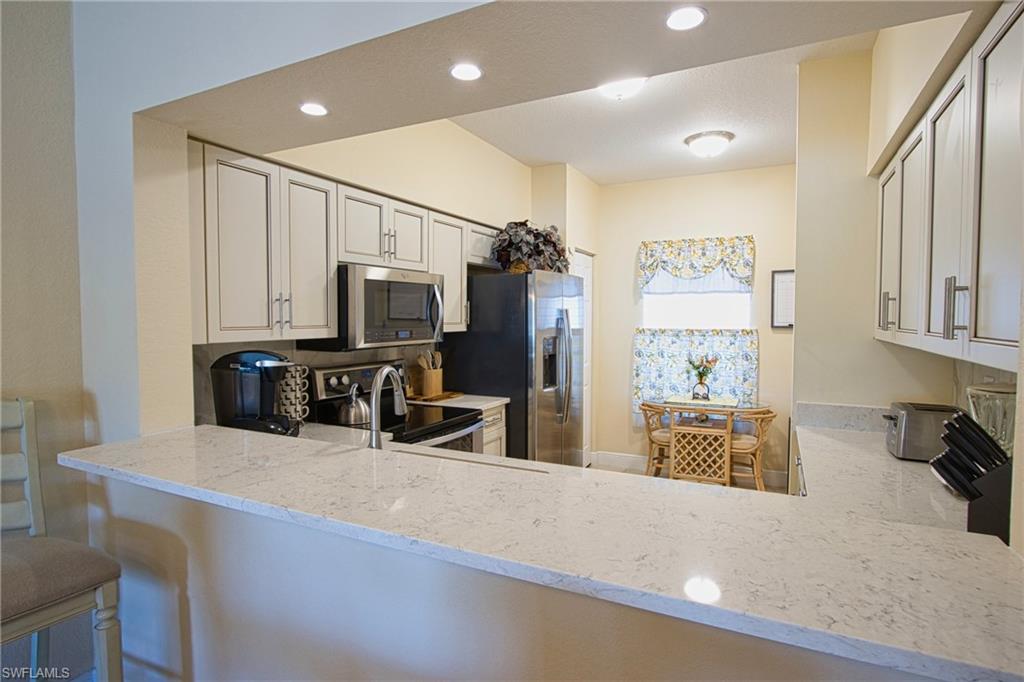 Kitchen with appliances with stainless steel finishes, white cabinets, kitchen peninsula, light stone counters, and a kitchen bar