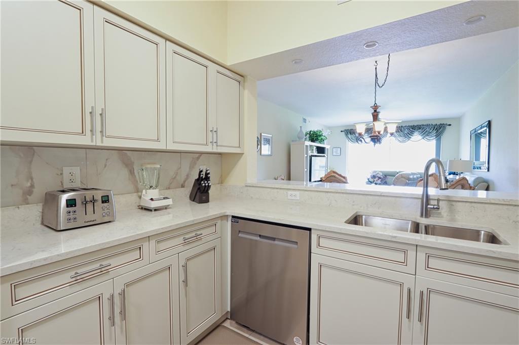 Kitchen featuring light stone countertops, dishwasher, an inviting chandelier, backsplash, and sink