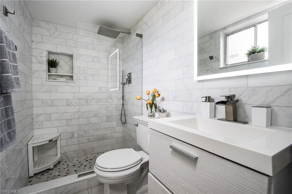 Bathroom featuring vanity, tasteful backsplash, a tile shower, tile walls, and toilet