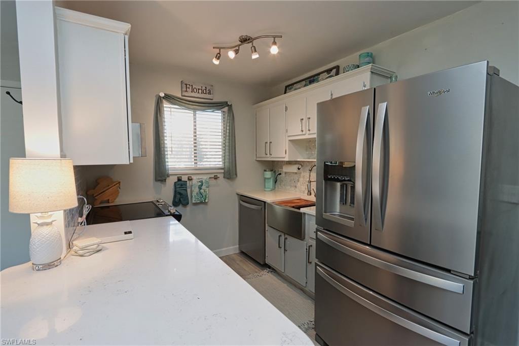 Kitchen featuring appliances with stainless steel finishes, white cabinetry, tasteful backsplash, light hardwood / wood-style flooring, and sink