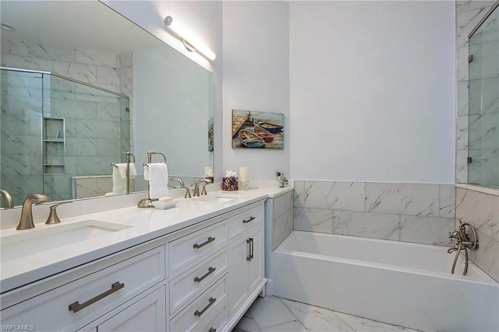 Bathroom featuring a bath, double vanity, light marble finish floors, and a marble finish shower