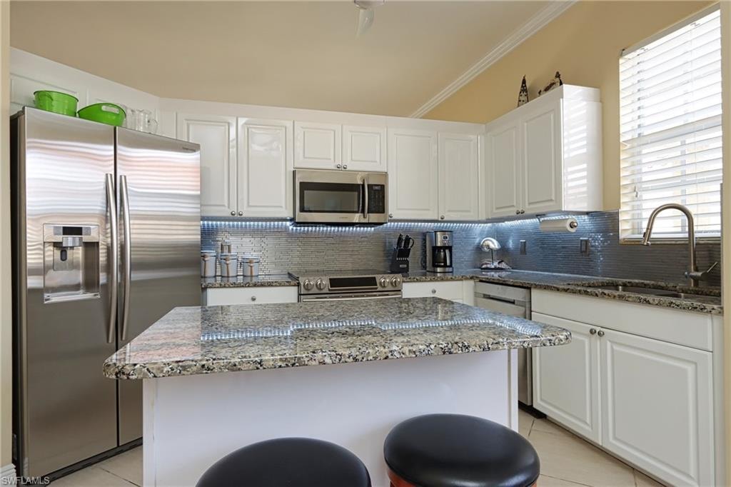 Kitchen with dark stone countertops, stainless steel appliances, backsplash, white cabinets, and light tile patterned flooring