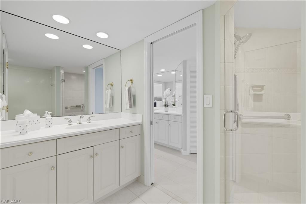 Spacious bathroom featuring a large vanity with ample counter space, full-width mirror, recessed lighting, and a walk-in shower with clear glass enclosure and grab bars