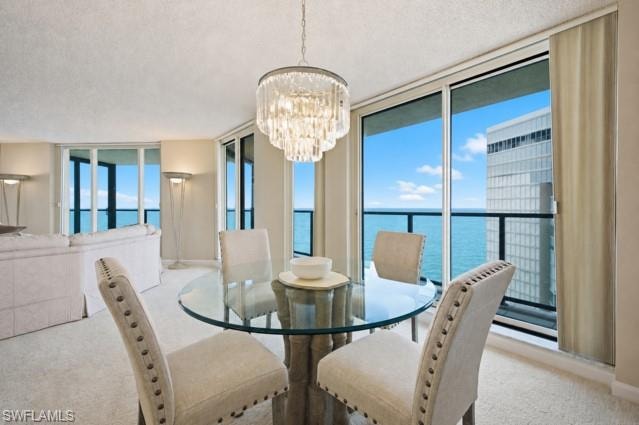 Dining area featuring a crystal chandelier, glass-top table, and sliding glass doors opening to a water scene
