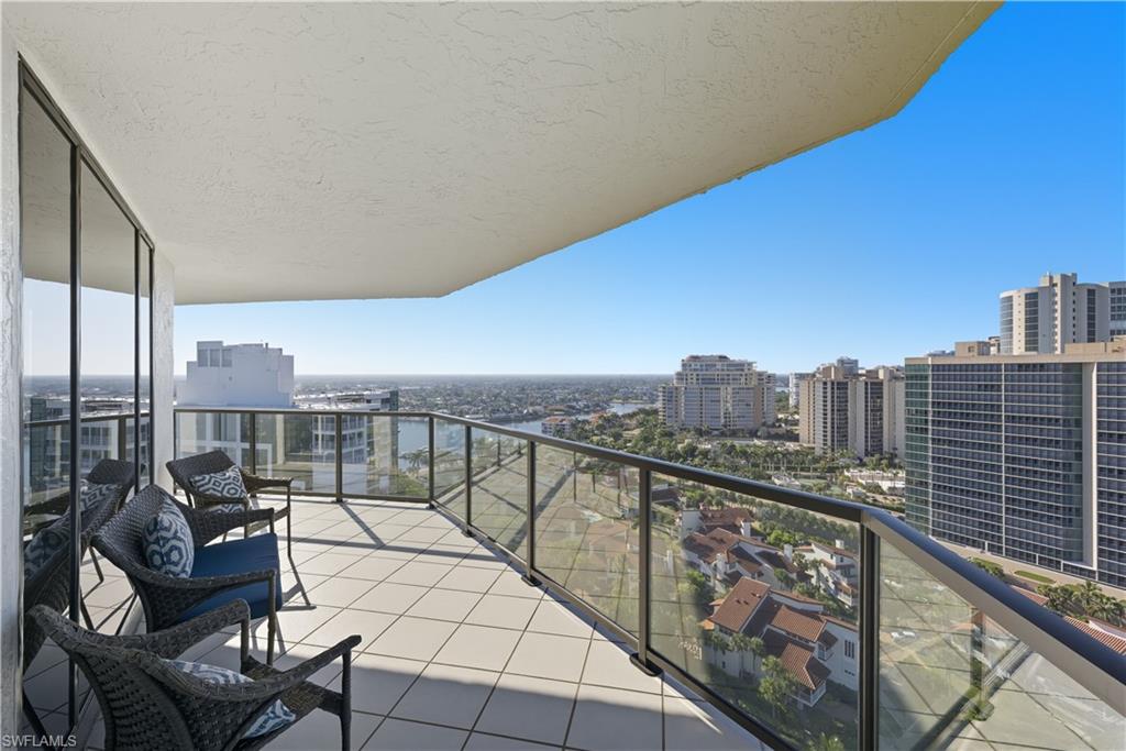 Expansive outdoor balcony featuring square tile flooring and a glass panel railing system with a dark frame