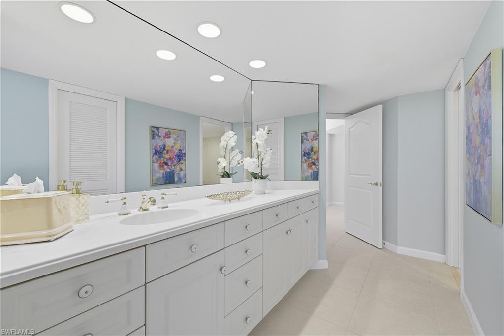 Spacious dual vanity featuring white cabinetry, integrated sinks, a generous countertop, and an expansive wall-mounted mirror