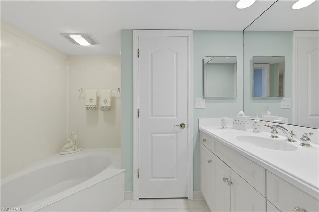 Bathroom featuring a built-in tub with shower surround, a white vanity with integrated sink, and a large wall-mounted mirror