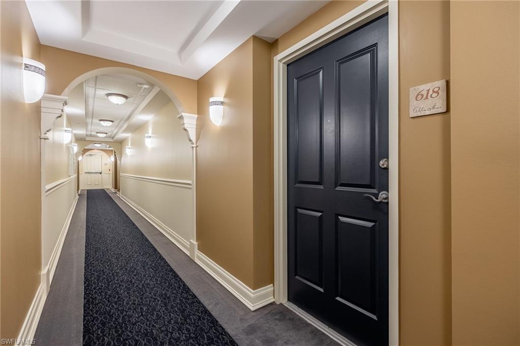 Hall featuring a raised ceiling, dark carpet, and ornate columns