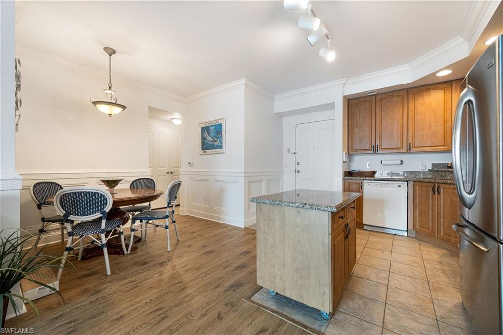 Kitchen with dishwasher, dark stone countertops, stainless steel fridge, hanging light fixtures, and a center island