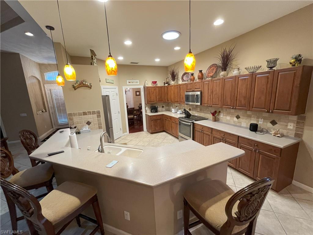 Expansive kitchen featuring a large island with sink, wood-finish cabinetry, tile flooring, and a tiled backsplash