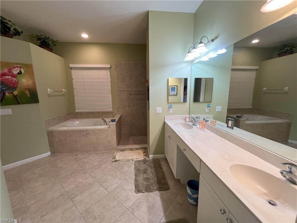 Spacious bathroom featuring a dual vanity with integrated sinks, a large mirror, a tiled soaking tub, a separate tiled shower enclosure, and neutral tile flooring