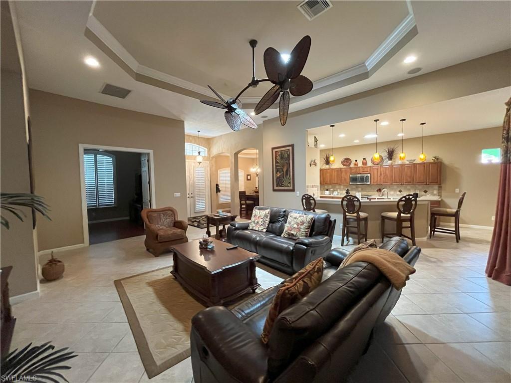 Spacious living area featuring tile flooring, a tray ceiling with a ceiling fan, and recessed lighting