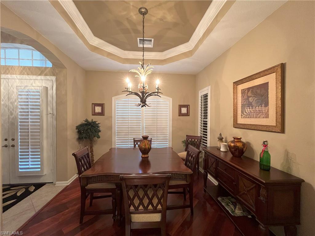 Dining area featuring a tray ceiling with crown molding, a decorative chandelier, and wood-finish flooring