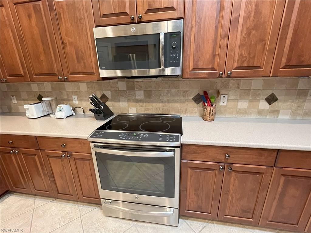 Kitchen featuring stainless steel range with ceramic cooktop, coordinating stainless steel microwave, extensive wood cabinetry, light-toned countertops, and a tiled backsplash with decorative accents