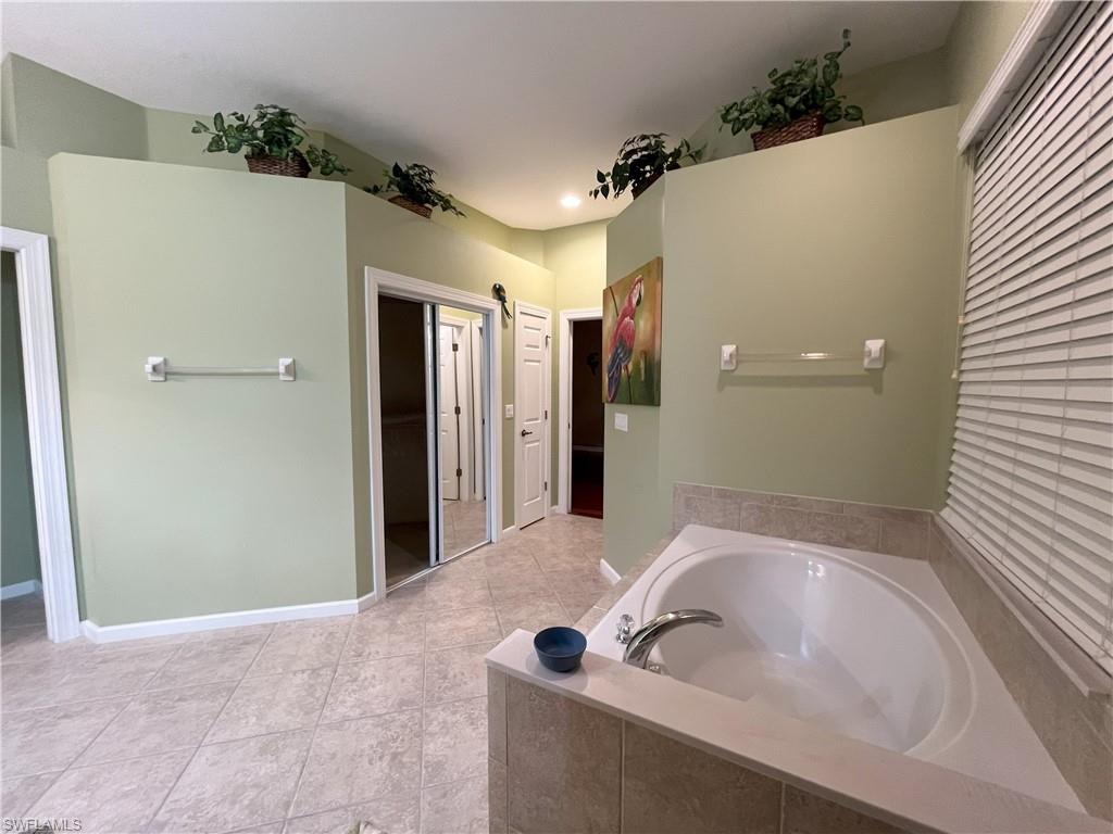 Spacious bathroom featuring an oval soaking tub with tiled surround, light-toned ceramic tile flooring, and a mirrored closet door