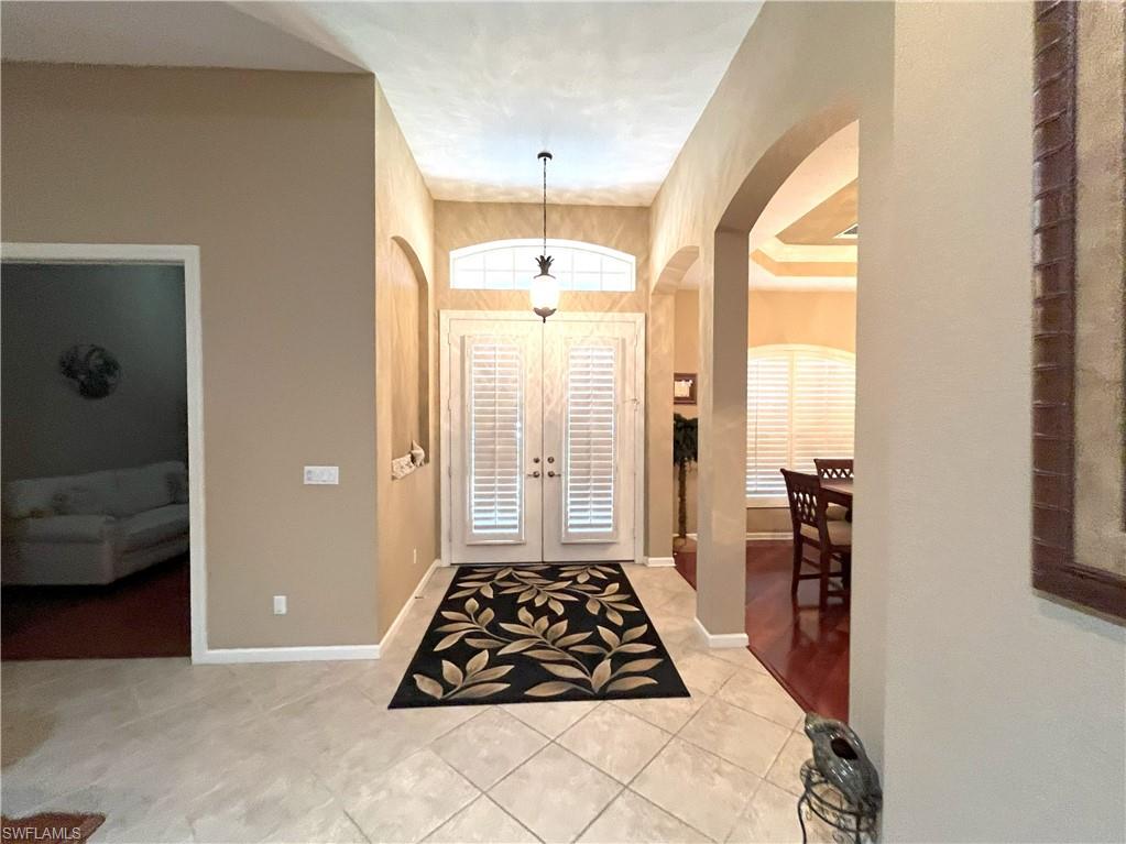Foyer featuring large format tile flooring, double entry doors with integrated louvered blinds, an arched transom window, and a central pendant light fixture