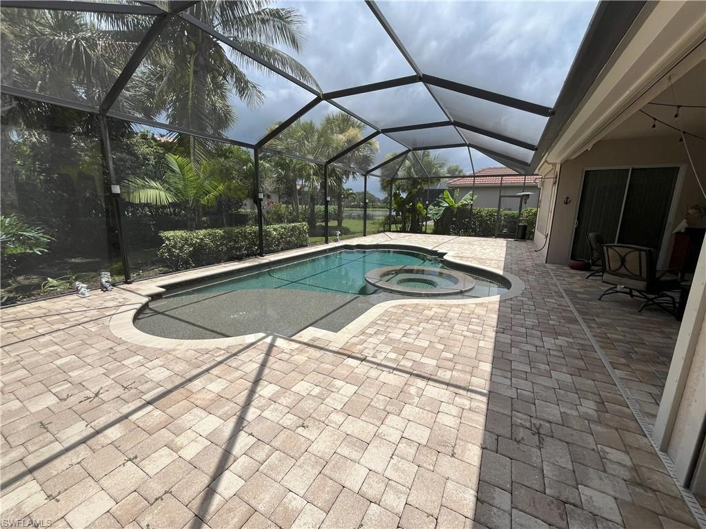 Screened enclosure featuring a freeform pool with integrated spa, paver deck, and lush tropical landscaping
