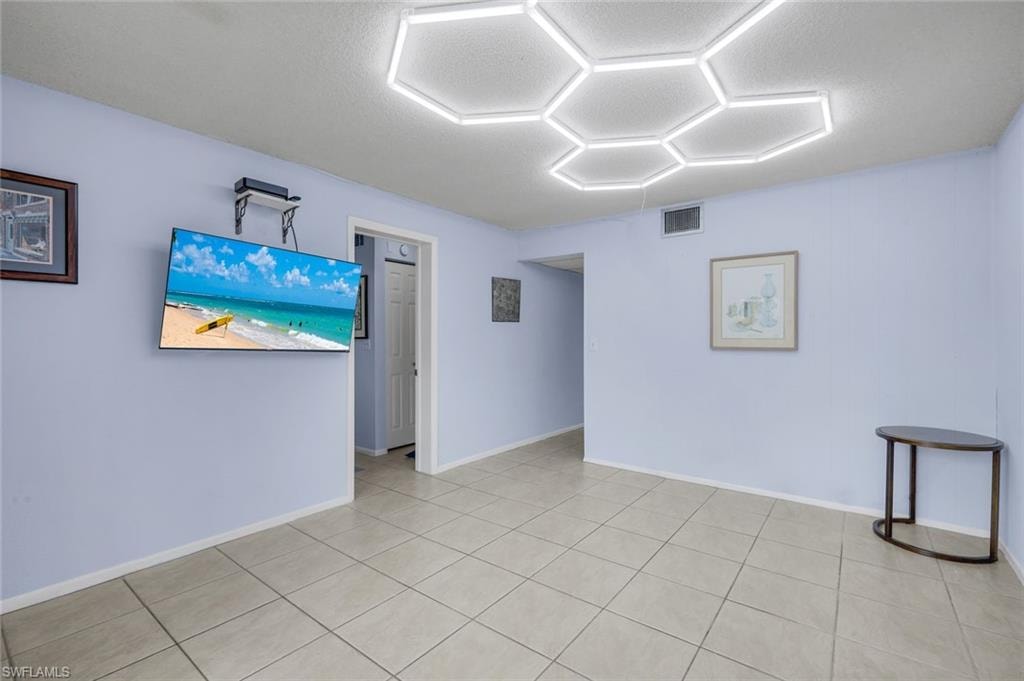 Living area featuring light-toned tile flooring, hexagonal ceiling lighting, and a wall-mounted flat-screen television