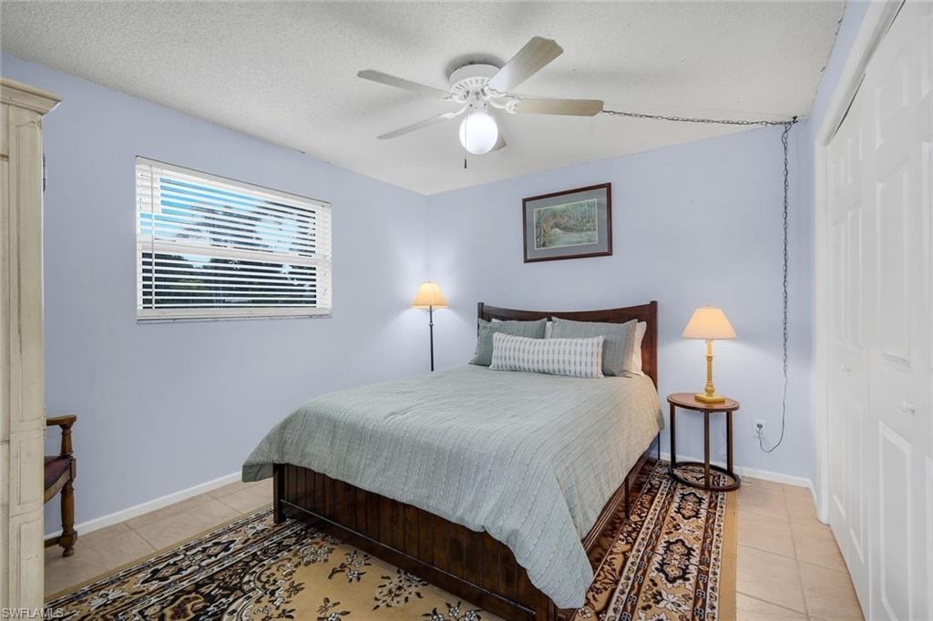 Bedroom featuring tile flooring, a window with horizontal blinds, a ceiling fan with integrated lighting, and bi-fold closet doors