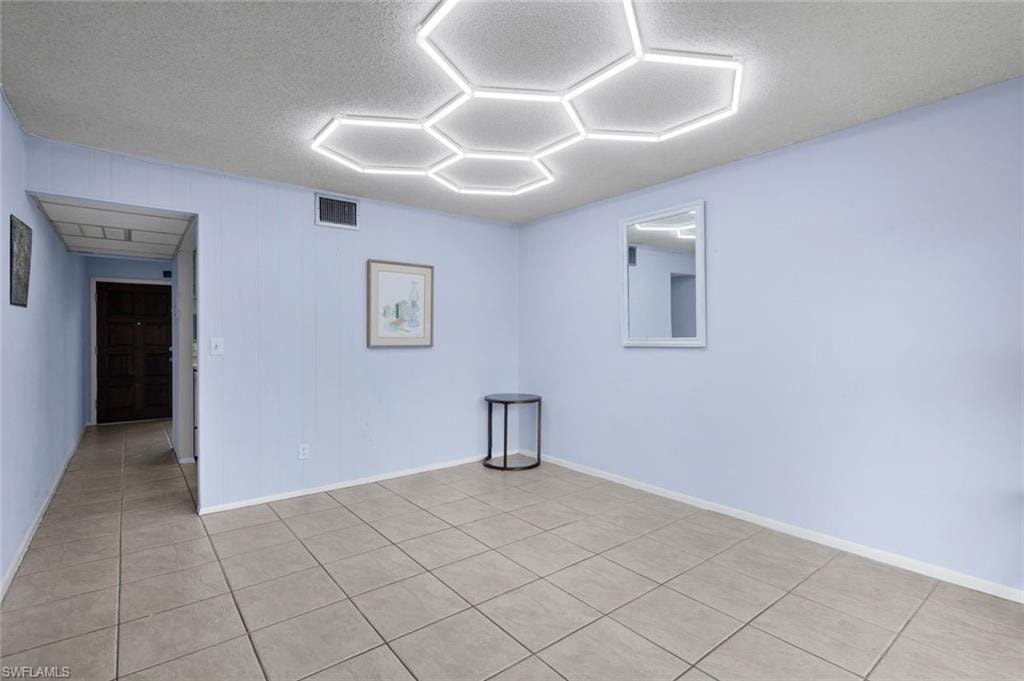Hexagonal ceiling light fixtures illuminate a room featuring light blue walls and neutral-toned tile flooring