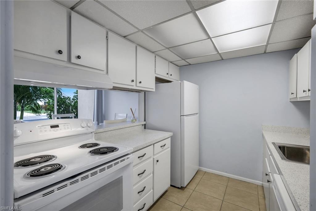 Kitchen featuring white cabinetry with black hardware, an electric range, a refrigerator, and a stainless steel sink