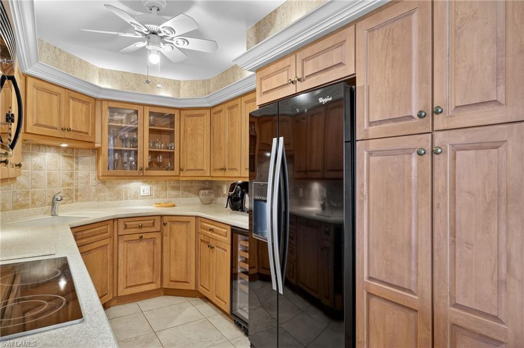 Kitchen with black refrigerator with ice dispenser, backsplash, electric stovetop, light tile patterned floors, and light countertops