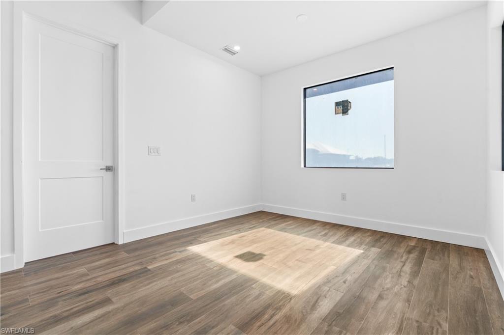 Room featuring wood-finish flooring, white baseboards, a flat-panel door with a brushed nickel handle, and a large rectangular window