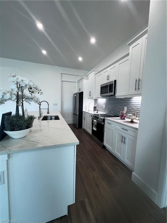 Gourmet kitchen featuring a substantial island with an integrated sink and light-toned countertop, wood-finish flooring, white shaker-style cabinetry, and stainless steel appliances